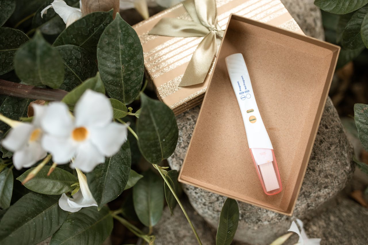 our-services-1 Pregnancy test placed in an open gift box surrounded by green leaves and white flowers.